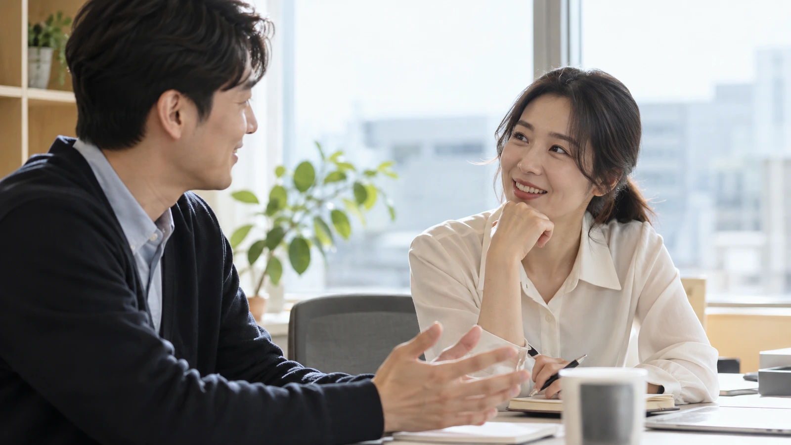 책상에서 펜을 든 여성과 손짓하는 남성이 서로 바라보며 대화하는 모습